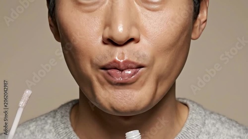 Close-Up Of A Person With Gap-Tooth Smile Applying Lip Gloss In Studio Setting With Plain Background