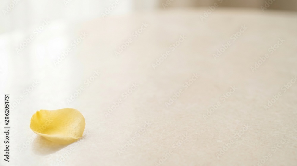 Obraz premium A single yellow rose petal rests on a polished surface, catching the soft light. The scene evokes a sense of delicate beauty and quiet reflection, with a hint of gentle fading or romance.