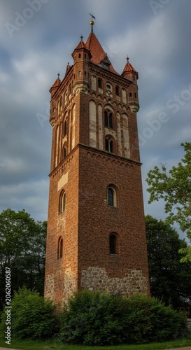 Historic brick water tower with red tiled roof against a cloudy sky.