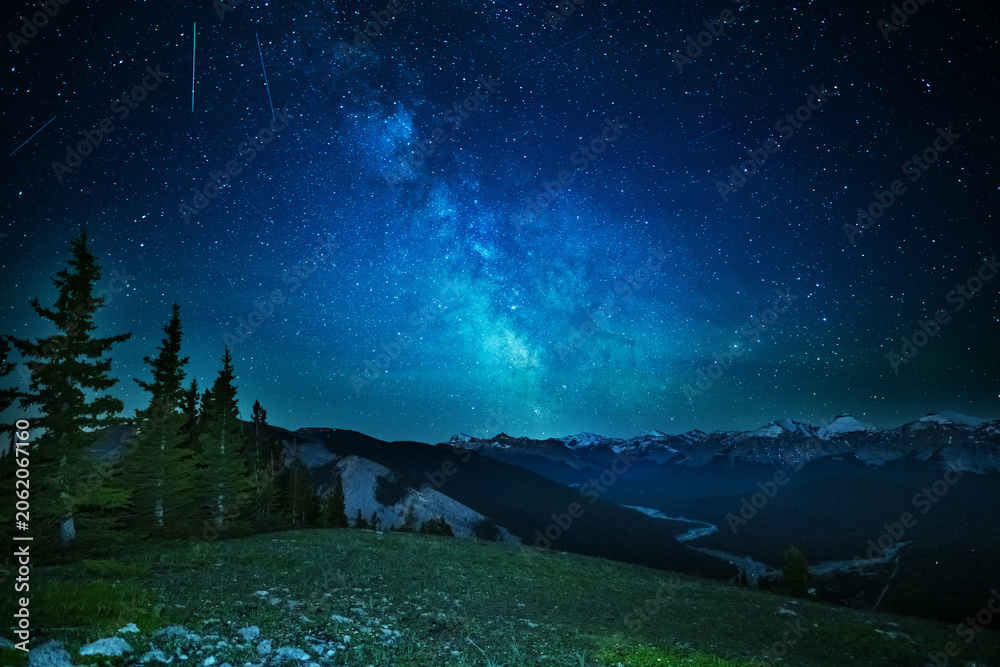 Fototapeta premium A clear, starry night with the Milky Way in the background, next to a camping tent and the rocky Canadian mountains 