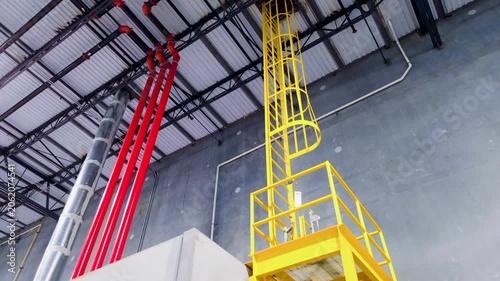 Fixed steel safety ladder with cage and maintenance platform in warehouse with utility pipes in metal ceiling
