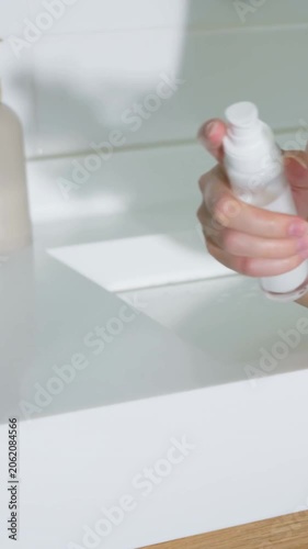 Vertical video: Pressing pump, hands with jade bangle applying lotion for skin at sink, copy space