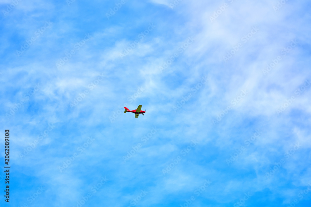 Fototapeta premium Small red airplane flying in clear blue sky with white clouds