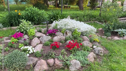Beautiful rose garden. A beautiful garden with a variety of bright flowers, including red, pink, white and yellow, surrounded by large stones and lush greenery on a manicured lawn.