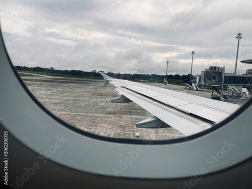 airplane wing seen through an oval passenger window parked at the airport tarmac
