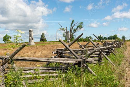 Split rail fences across green fields at Gettysburg National Military Park in Gettysburg, Pennsylvania, USA, under blue sky with clouds.