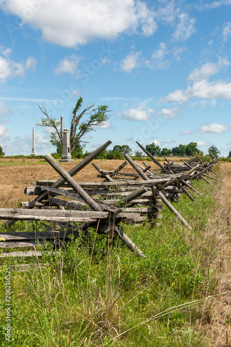 Split rail fences across green fields at Gettysburg National Military Park in Gettysburg, Pennsylvania, USA, under blue sky with clouds.