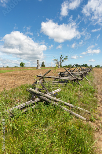 Split rail fences across green fields at Gettysburg National Military Park in Gettysburg, Pennsylvania, USA, under blue sky with clouds.