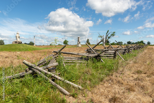 Split rail fences across green fields at Gettysburg National Military Park in Gettysburg, Pennsylvania, USA, under blue sky with clouds.