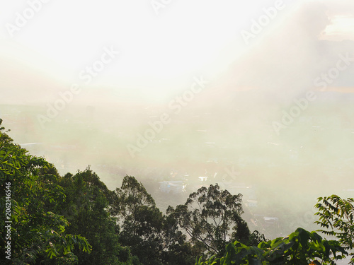 Industrial smog or burning waste pollutants drift into the air, affecting the atmosphere and the sun. Buildings and trees obstruct the view, reducing visibility.