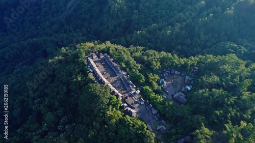 Aerial view of Bena Traditional Village with its iconic thatched roof houses surrounded by lush green forest in Kecamatan Jerebuu, Nusa Tenggara Timur, Indonesia.
