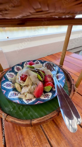 Close-up of authentic Thai spicy papaya salad or call Somtum and crispy pork cracklings platter set on wooden table by river