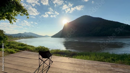Sunburst over mountain river with empty camping chair on deck