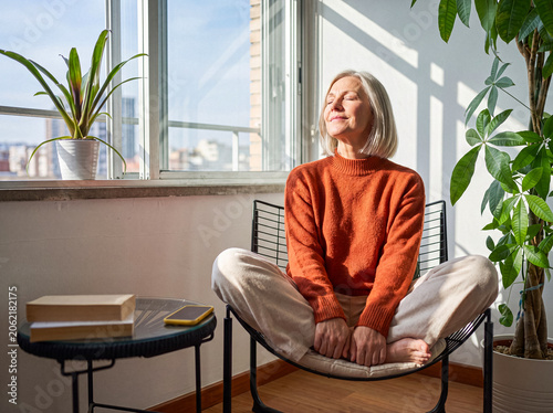 Tableau sur toile Content senior woman with closed eyes enjoying warm sunlight indoors, meditating or relaxing in peaceful home