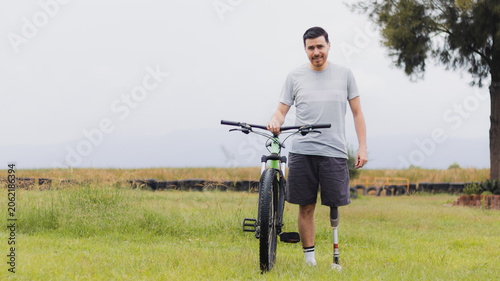 Obraz na płótnie Confident adaptive athlete with a lower-limb prosthetic leg standing beside a mountain bike in an open grassy field