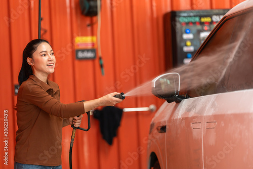 Obraz na plátně woman washing car with water hose in a self-service car wash station