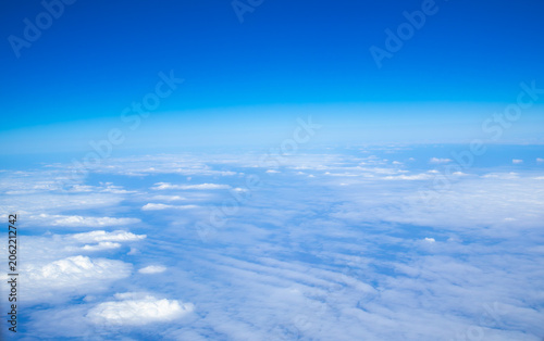Beautiful aerial view of a cloud layer seen from an airplane at cruising altitude. Blue sky above and soft white clouds below create a peaceful atmosphere during a daytime flight.