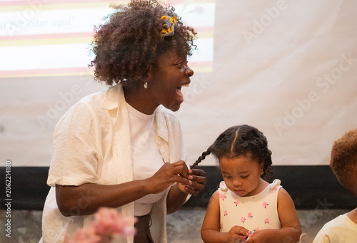 Tableau sur toile Mother braiding her smiling young daughter's hair, showing family togetherness a