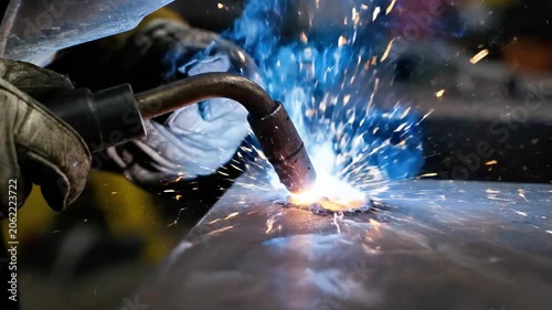 A close-up of a gloved hand holding a welding torch with sparks flying