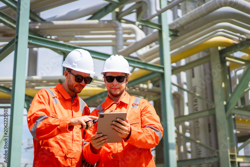 Refinery workers checking pipeline data on a digital tablet outdoors
