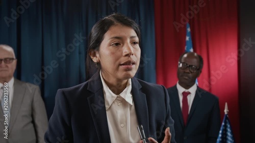 Young Hispanic woman politician speaking at podium, gesturing during press conference with diverse colleagues. Footage is suitable for political campaigns or news broadcasts