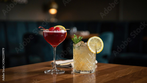 Two elegant colorful cocktails served in fancy glassware on a polished wooden bar top surface