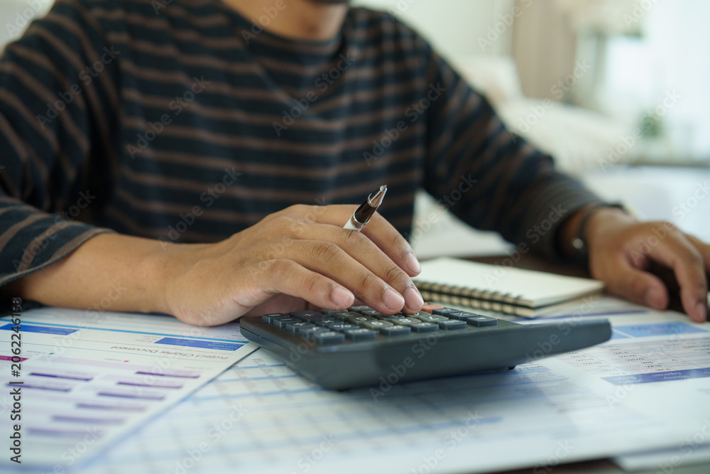 Fototapeta premium Person using a calculator with financial documents at home, concept of budgeting, expense planning, savings, and household money management.