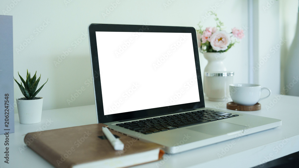 Fototapeta premium Laptop mockup with blank white screen on a clean desk, decorated with notebook, pen, plant, coffee cup, and flowers.