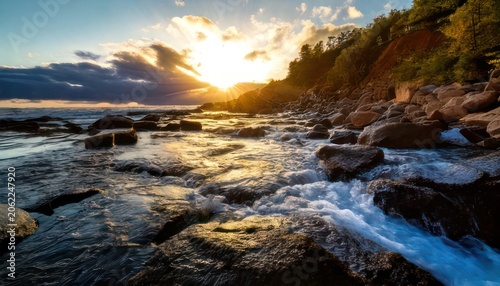Coastal Serenity - Sunlit Waves and Rocky Shoreline at Dusk.