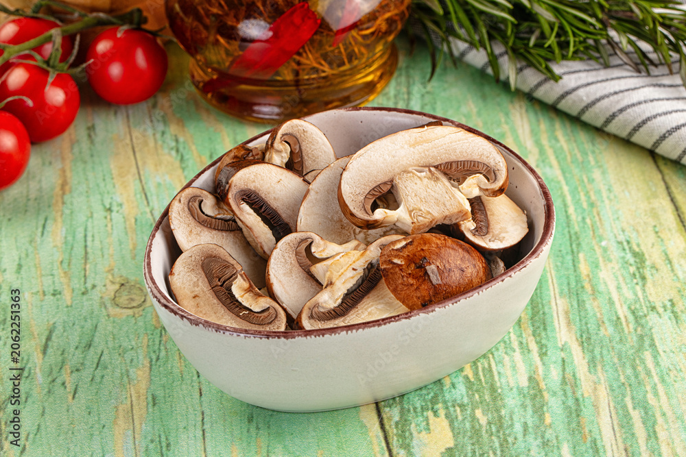 Fototapeta premium Sliced mushrooms in ceramic bowl with tomatoes and rosemary on rustic green wooden table