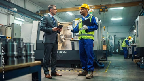 Engineer and manager discussing technical production project in modern manufacturing machine shop.