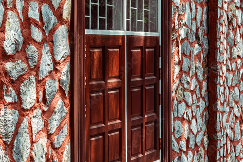 Vintage building facade with stone wall and wooden windows. Exterior view of vintage building featuring beautifully textured stone masonry wall. traditional wooden panel windows with white frames.