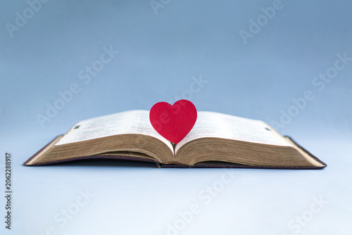 Open bible with a red heart at the center of the pages. Isolated on light blue background.
