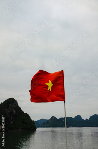Tableau sur toile Vietnamese flag on Halong Bay boat: red flag with golden star flies proudly, calm waters surround majestic karst formations, blending national pride with serene natural beauty in iconic landscape