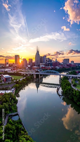 A serene cityscape at sunset, featuring a river with a bridge and lush greenery