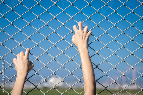 Obraz na płótnie Closeup of a human hand gripping a chain link fence as if trying to escape, representing border control, imprisonment, human trafficking, and the fight against restricted movement and injustice