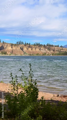 Vertical format of water with some barren land. Windy day with leaves blowing and small waves washing up onto the shore. Hoodoos can be seen in the distance.