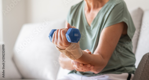 Person wearing a wrist brace on injured hand while lifting a small dumbbell, performing exercises for rehabilitation and physical therapy at home