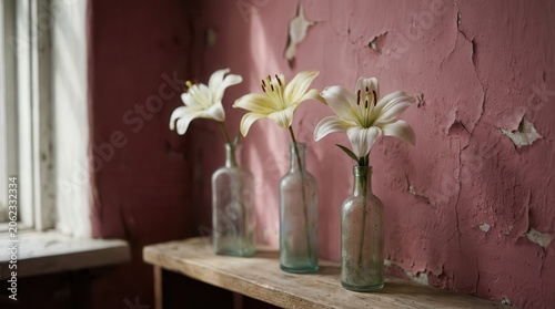 Three white and yellow lilies in vintage glass bottles on a rustic shelf, against a textured pink wall with peeling paint.