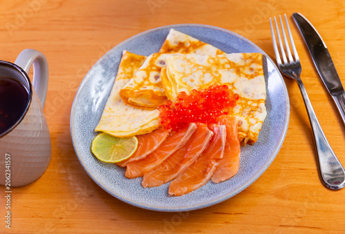 Crepes cooked in butter are served with red caviar, sliced salmon and a slice of lemon. Serving delicious pancakes with fish