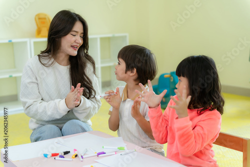 Happy kindergarten children and teacher playing a hand clapping game together in classroom
