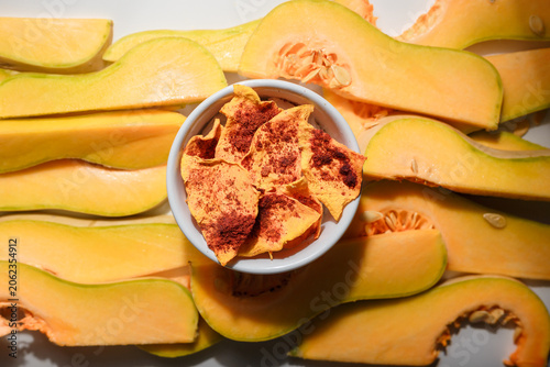 Autumn superfood. Raw and dehydrated crispy pumpkin chips in bowl and white background. Product presentation