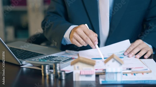 Businessman analyzing financial charts, counting coins, and using a calculator to evaluate asset sales and profits.