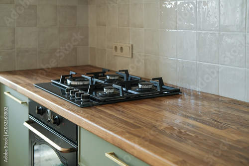 Modern kitchen interior featuring a wooden countertop, open wall shelves and built-in gas cooktop. Minimalist residential design with light cabinetry, tiled backsplash and contemporary home decor.