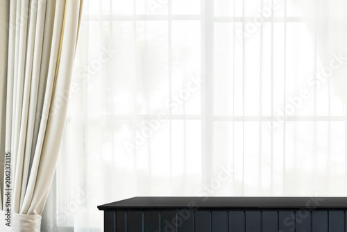 A black wooden table, with a background of brown curtains and translucent curtains