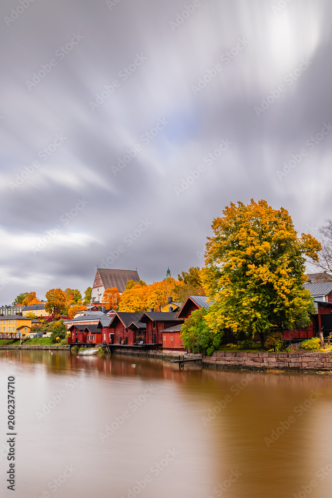 Fototapeta premium Scenic autumn view of Old Porvoo, Finland, featuring colorful traditional wooden houses and the Porvoo Cathedral overlooking the river, framed by golden reeds in the foreground.
