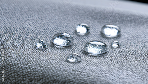 Water beads persist on a fabric surface. The material exhibits a texture that repels liquid, forming a barrier. This characteristic demonstrates textile resistance to moisture and marks.