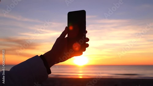 Hands Holding Smartphone at Sunset Over Calm Ocean