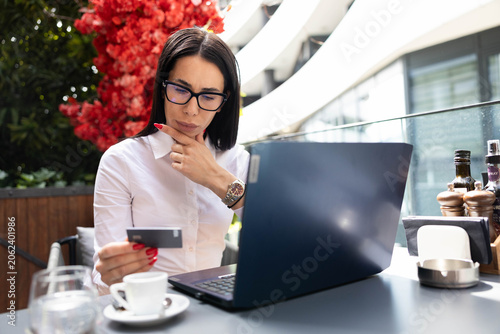 Konstfotografi Woman wearing glasses sitting at a cafe, holding a credit card and looking at a