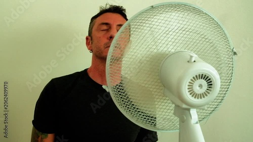 A man enjoys the coolness of the fan up close to counteract the summer heat. The man in the video is forty-two years old, is an Italian of Caucasian origin and wears a dark gray T-shirt